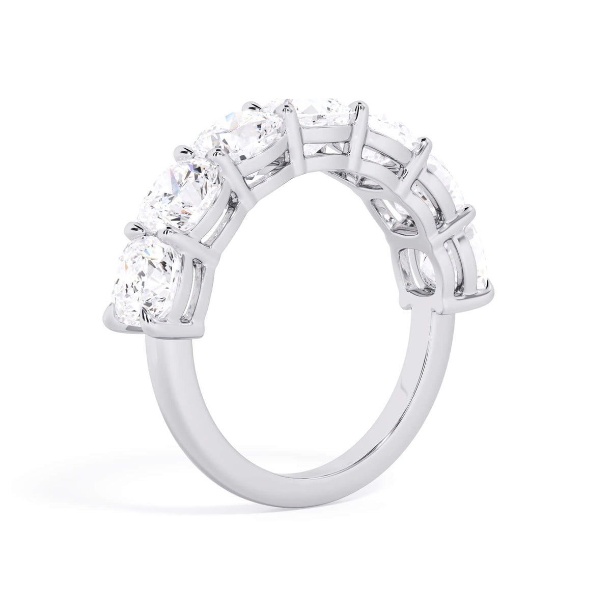 A picture of a seven stone diamond wedding ring with cushion cut diamonds that are shared prong set in white gold or platinum on a white background with a slightly angled, through the finger view.