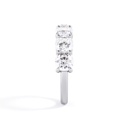A picture of a seven stone diamond wedding ring with cushion cut diamonds that are shared prong set in white gold or platinum on a white background with a side profile view.