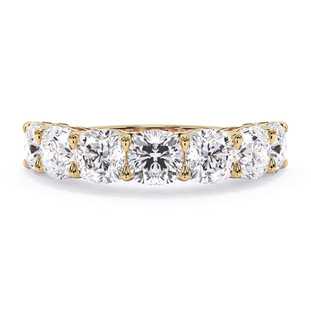 A picture of a seven stone diamond wedding ring with cushion cut diamonds that are shared prong set in yellow gold on a white background with the ring facing forward, lying down.