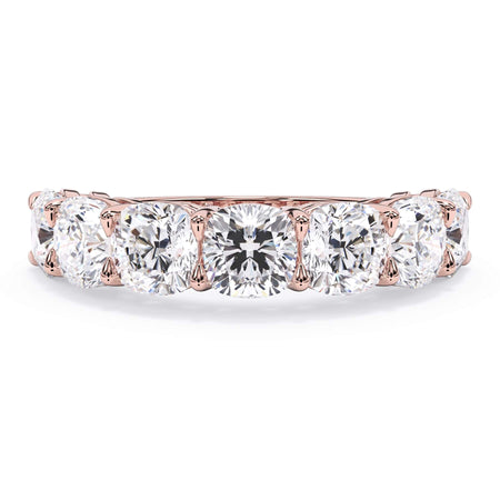 A picture of a seven stone diamond wedding ring with cushion cut diamonds that are shared prong set in rose gold on a white background with the ring facing forward, lying down.