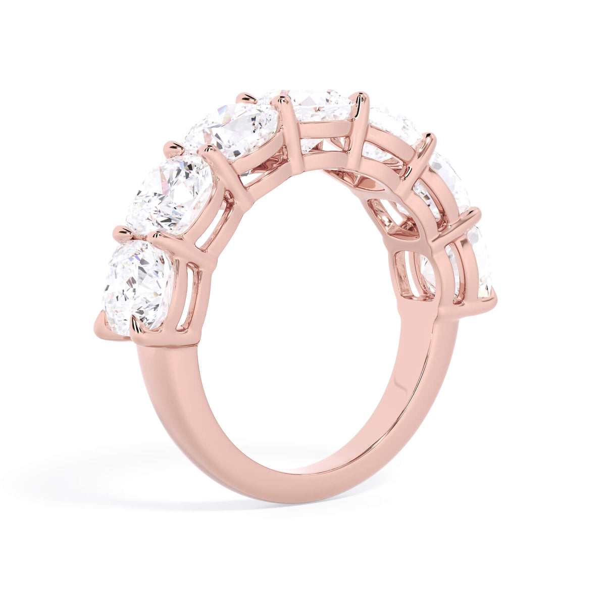 A picture of a seven stone diamond wedding ring with cushion cut diamonds that are shared prong set in rose gold on a white background with a slightly angled, through the finger view.