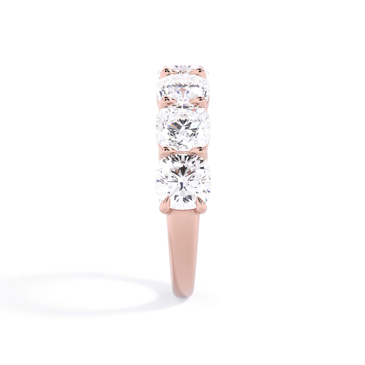 A picture of a seven stone diamond wedding ring with cushion cut diamonds that are shared prong set in rose gold on a white background with a side profile view.