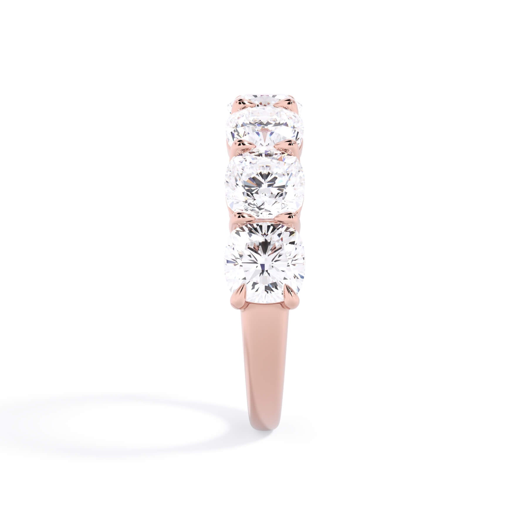 A picture of a seven stone diamond wedding ring with cushion cut diamonds that are shared prong set in rose gold on a white background with a side profile view.