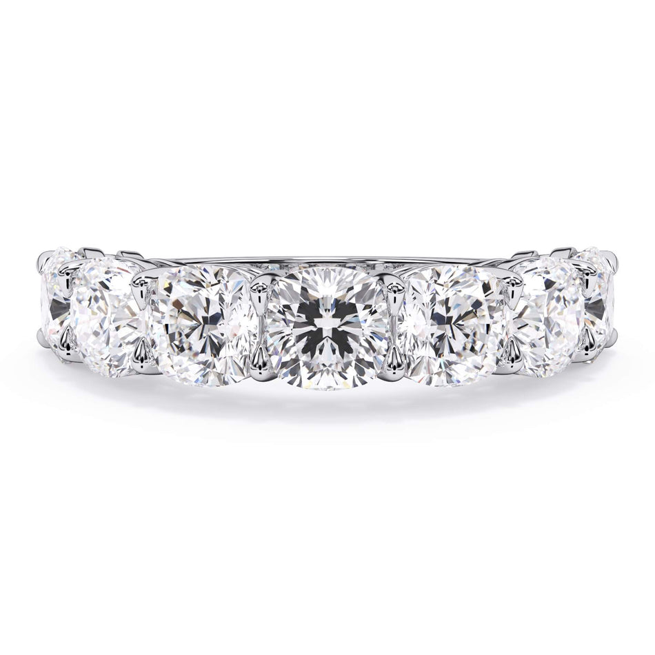A picture of a seven stone diamond wedding ring with cushion cut diamonds that are shared prong set in white gold or platinum on a white background with the ring facing forward, lying down.