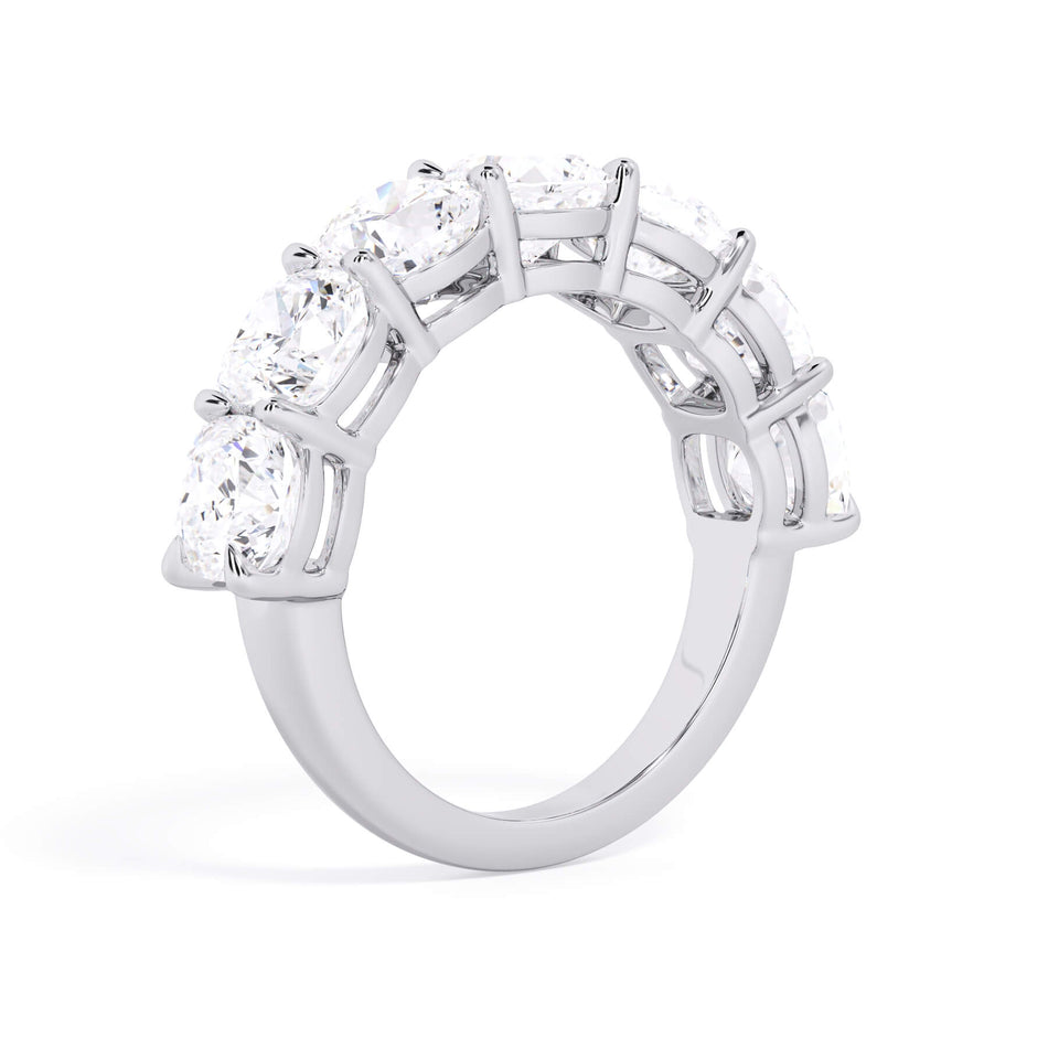 A picture of a seven stone diamond wedding ring with cushion cut diamonds that are shared prong set in white gold or platinum on a white background with a slightly angled, through the finger view.