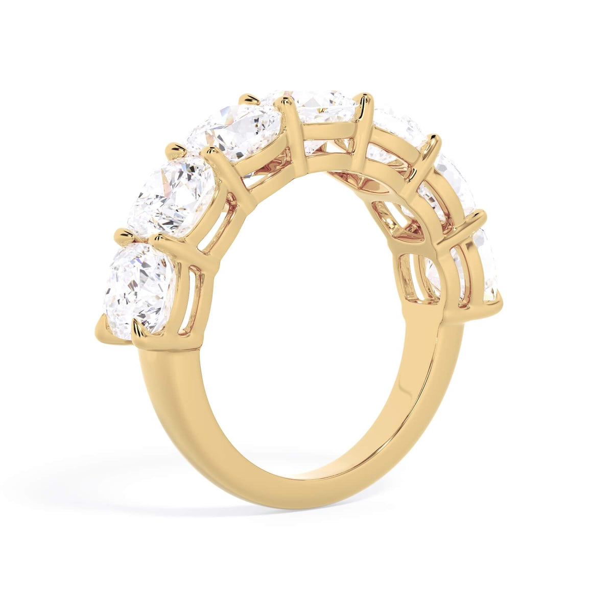 A picture of a seven stone diamond wedding ring with cushion cut diamonds that are shared prong set in yellow gold on a white background with a slightly angled, through the finger view.