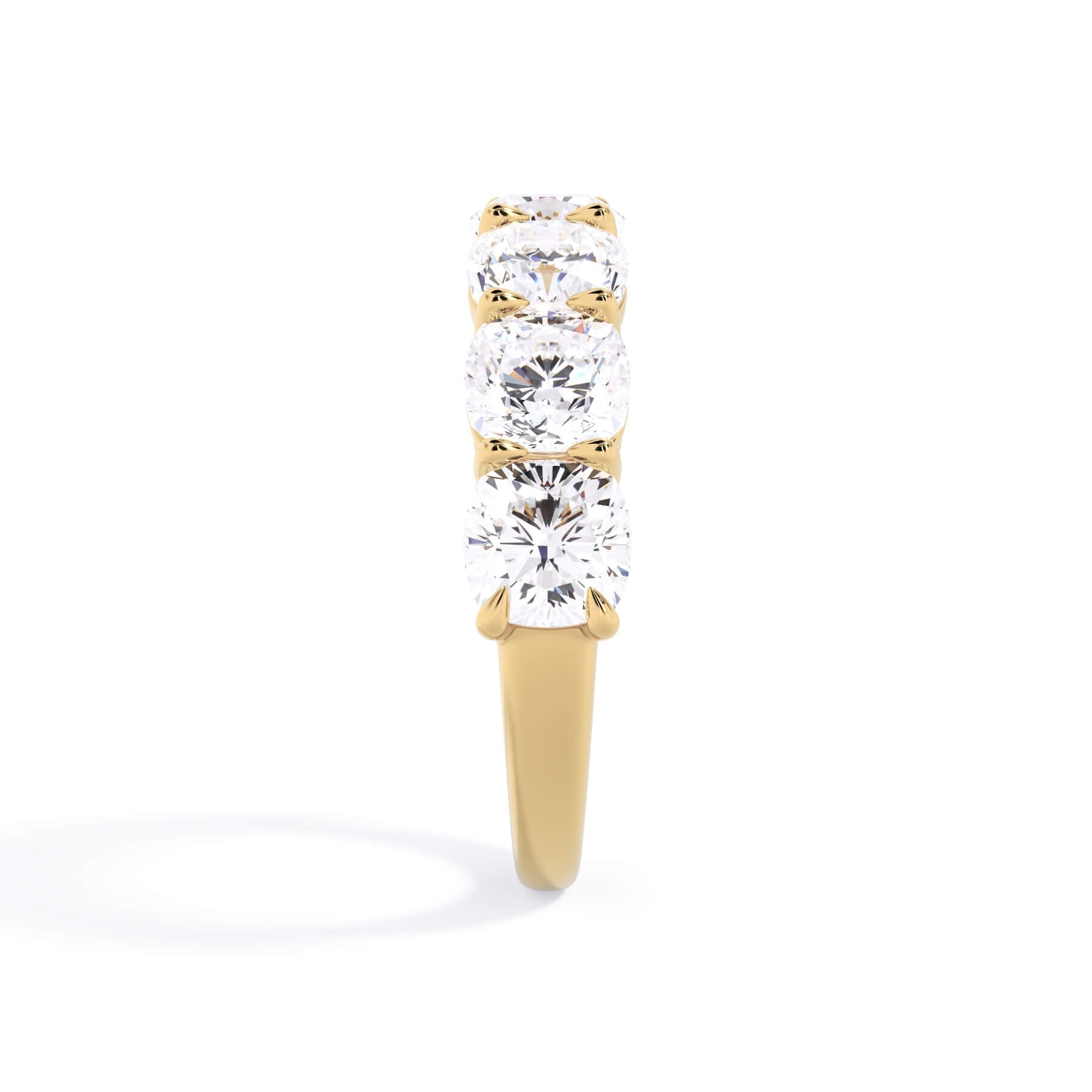 A picture of a seven stone diamond wedding ring with cushion cut diamonds that are shared prong set in yellow gold on a white background with a side profile view.