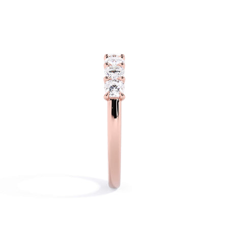 A picture of a seven stone diamond wedding ring with cushion cut diamonds that are U prong set in rose gold on a white background with a side profile view.