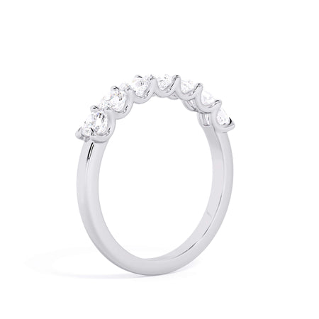 A picture of a seven stone diamond wedding ring with cushion cut diamonds that are U prong set in white gold or platinum on a white background with a slightly angled, through the finger view.
