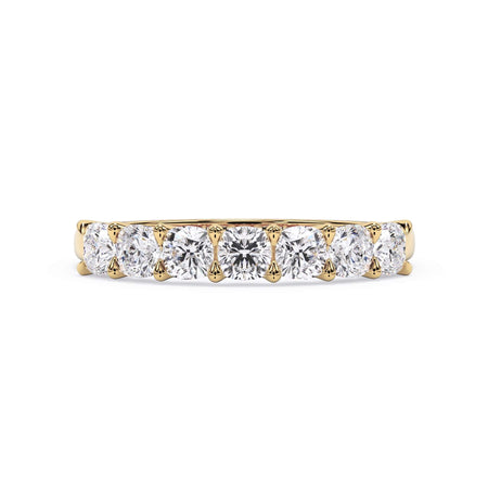 A picture of a seven stone diamond wedding ring with cushion cut diamonds that are U prong set in yellow gold on a white background with the ring facing forward, lying down.