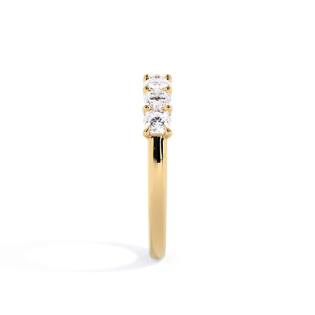 A picture of a seven stone diamond wedding ring with cushion cut diamonds that are U prong set in yellow gold on a white background with a side profile view.