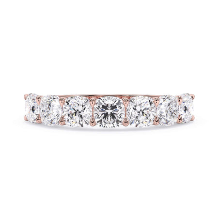 A picture of a seven stone diamond wedding ring with cushion cut diamonds that are U prong set in rose gold on a white background with the ring facing forward, lying down.
