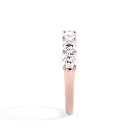 A picture of a seven stone diamond wedding ring with cushion cut diamonds that are U prong set in rose gold on a white background with a side profile view.