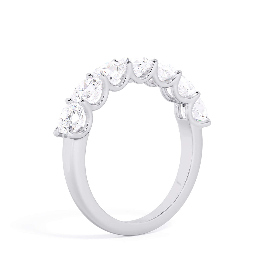 A picture of a seven stone diamond wedding ring with cushion cut diamonds that are U prong set in white gold or platinum on a white background with a slightly angled, through the finger view.