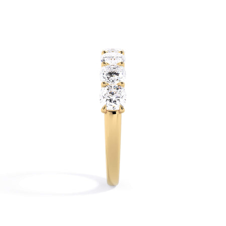 A picture of a seven stone diamond wedding ring with cushion cut diamonds that are U prong set in yellow gold on a white background with a side profile view.