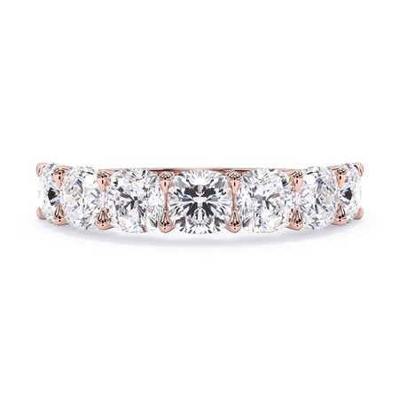 A picture of a seven stone diamond wedding ring with cushion cut diamonds that are U prong set in rose gold on a white background with the ring facing forward, lying down.