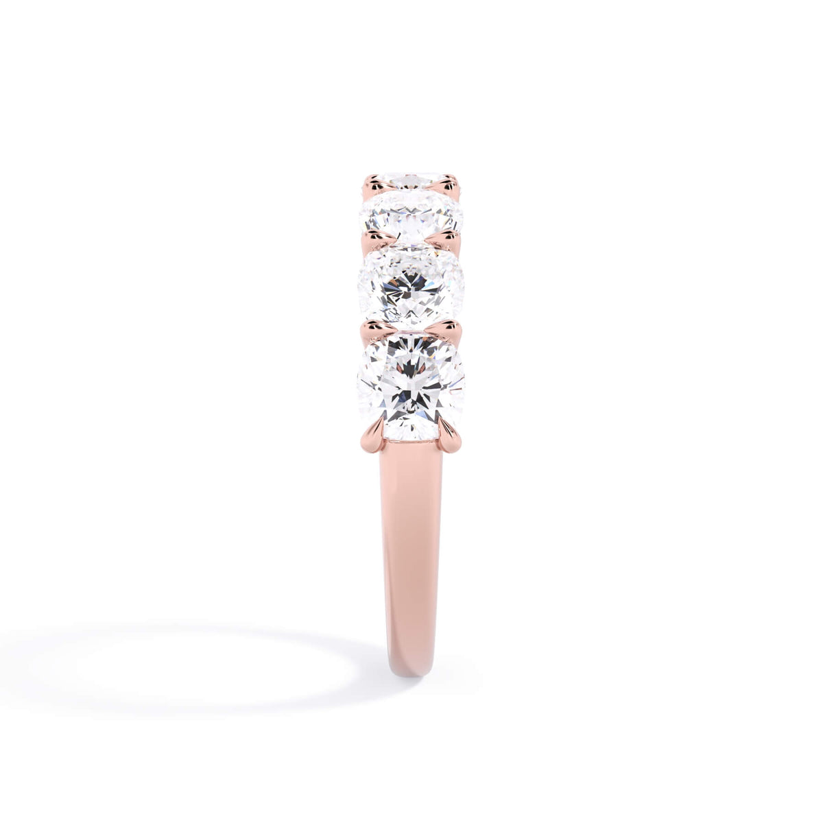 A picture of a seven stone diamond wedding ring with cushion cut diamonds that are U prong set in rose gold on a white background with a side profile view.