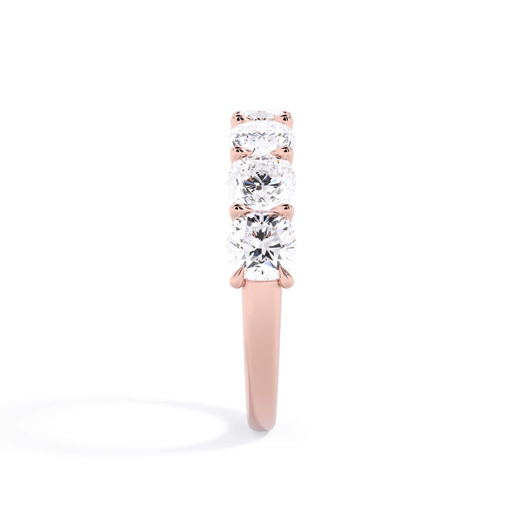 A picture of a seven stone diamond wedding ring with cushion cut diamonds that are U prong set in rose gold on a white background with a side profile view.