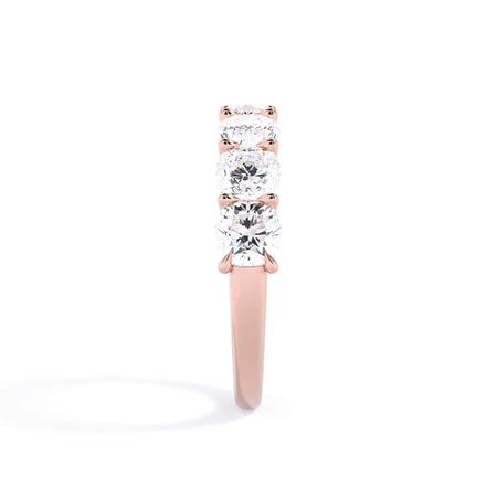 A picture of a seven stone diamond wedding ring with cushion cut diamonds that are U prong set in rose gold on a white background with a side profile view.