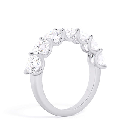 A picture of a seven stone diamond wedding ring with cushion cut diamonds that are U prong set in white gold or platinum on a white background with a slightly angled, through the finger view.