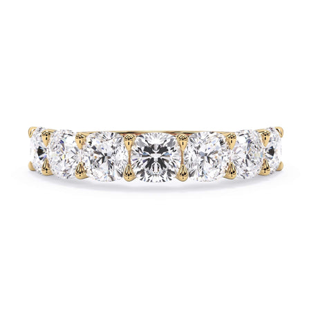 A picture of a seven stone diamond wedding ring with cushion cut diamonds that are U prong set in yellow gold on a white background with the ring facing forward, lying down.