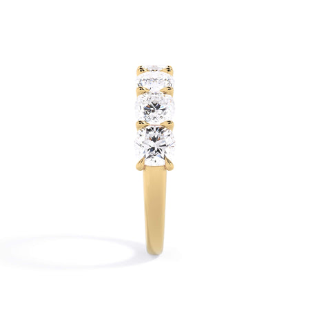 A picture of a seven stone diamond wedding ring with cushion cut diamonds that are U prong set in yellow gold on a white background with a side profile view.