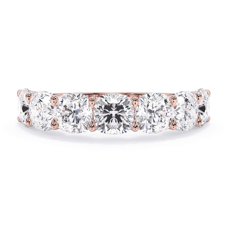 A picture of a seven stone diamond wedding ring with cushion cut diamonds that are U prong set in rose gold on a white background with the ring facing forward, lying down.