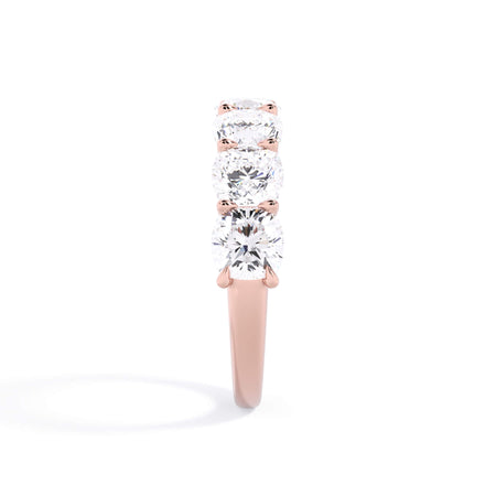 A picture of a seven stone diamond wedding ring with cushion cut diamonds that are U prong set in rose gold on a white background with a side profile view.