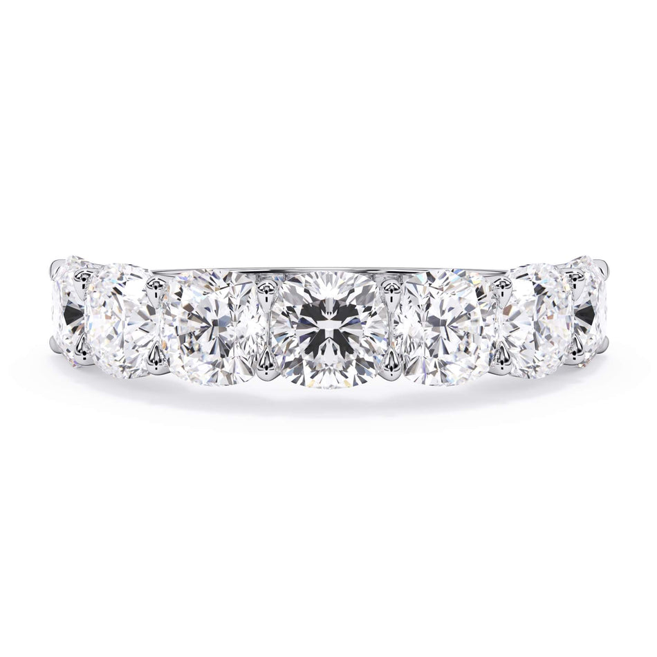 A picture of a seven stone diamond wedding ring with cushion cut diamonds that are U prong set in white gold or platinum on a white background with the ring facing forward, lying down.