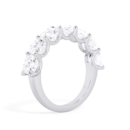 A picture of a seven stone diamond wedding ring with cushion cut diamonds that are U prong set in white gold or platinum on a white background with a slightly angled, through the finger view.