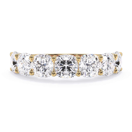 A picture of a seven stone diamond wedding ring with cushion cut diamonds that are U prong set in yellow gold on a white background with the ring facing forward, lying down.