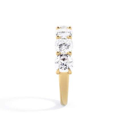 A picture of a seven stone diamond wedding ring with cushion cut diamonds that are U prong set in yellow gold on a white background with a side profile view.
