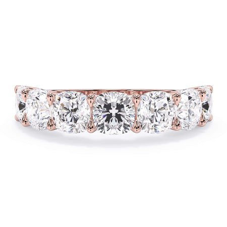 A picture of a seven stone diamond wedding ring with cushion cut diamonds that are U prong set in rose gold on a white background with the ring facing forward, lying down.