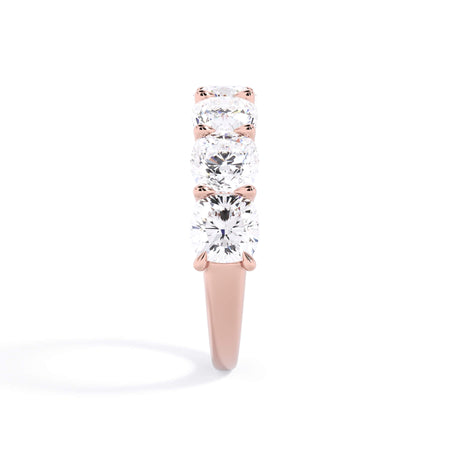 A picture of a seven stone diamond wedding ring with cushion cut diamonds that are U prong set in rose gold on a white background with a side profile view.