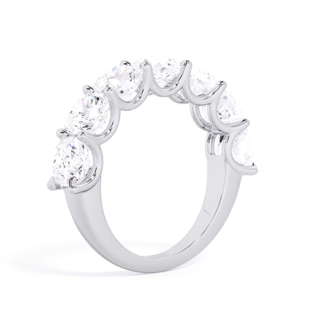 A picture of a seven stone diamond wedding ring with cushion cut diamonds that are U prong set in white gold or platinum on a white background with a slightly angled, through the finger view.