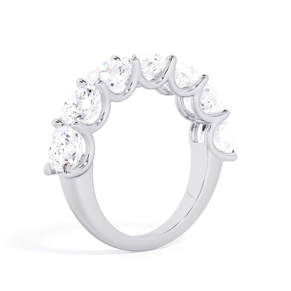 A picture of a seven stone diamond wedding ring with cushion cut diamonds that are U prong set in white gold or platinum on a white background with a slightly angled, through the finger view.