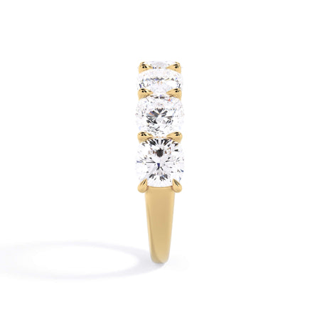 A picture of a seven stone diamond wedding ring with cushion cut diamonds that are U prong set in yellow gold on a white background with a side profile view.