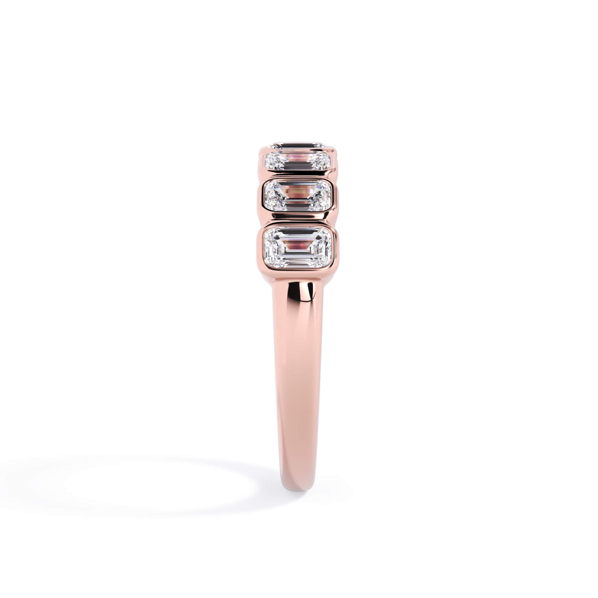 A picture of a seven stone diamond wedding ring with emerald cut diamonds that are bezel set in rose gold on a white background with a side profile view.