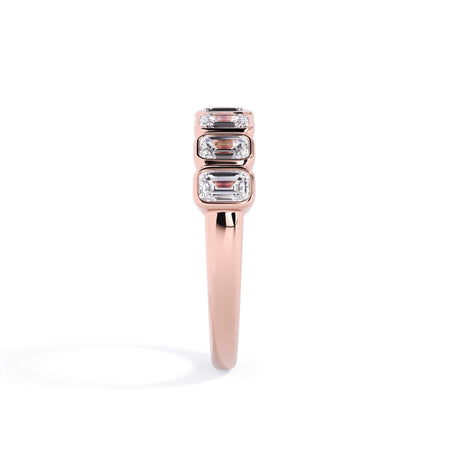 A picture of a seven stone diamond wedding ring with emerald cut diamonds that are bezel set in rose gold on a white background with a side profile view.