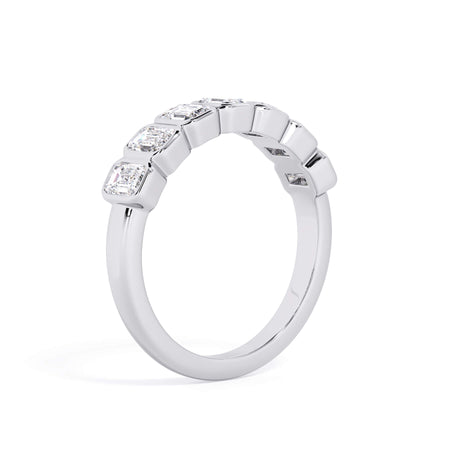 A picture of a seven stone diamond wedding ring with emerald cut diamonds that are bezel set in white gold or platinum on a white background with a slightly angled, through the finger view.