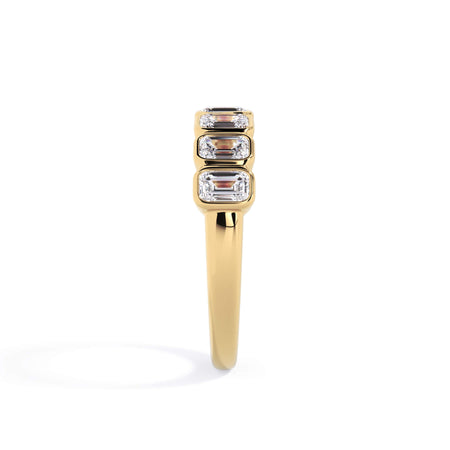 A picture of a seven stone diamond wedding ring with emerald cut diamonds that are bezel set in yellow gold on a white background with a side profile view.