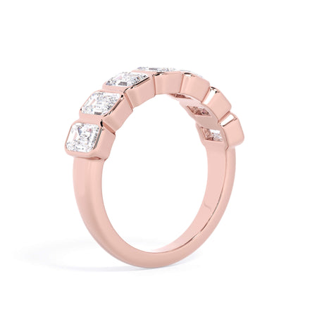A picture of a seven stone diamond wedding ring with emerald cut diamonds that are bezel set in rose gold on a white background with a slightly angled, through the finger view.