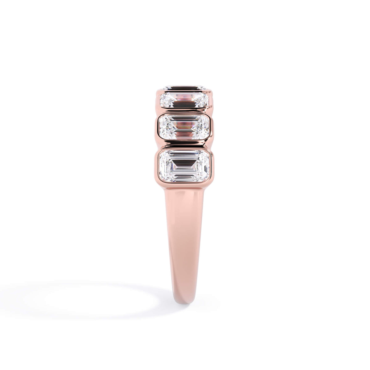 A picture of a seven stone diamond wedding ring with emerald cut diamonds that are bezel set in rose gold on a white background with a side profile view.