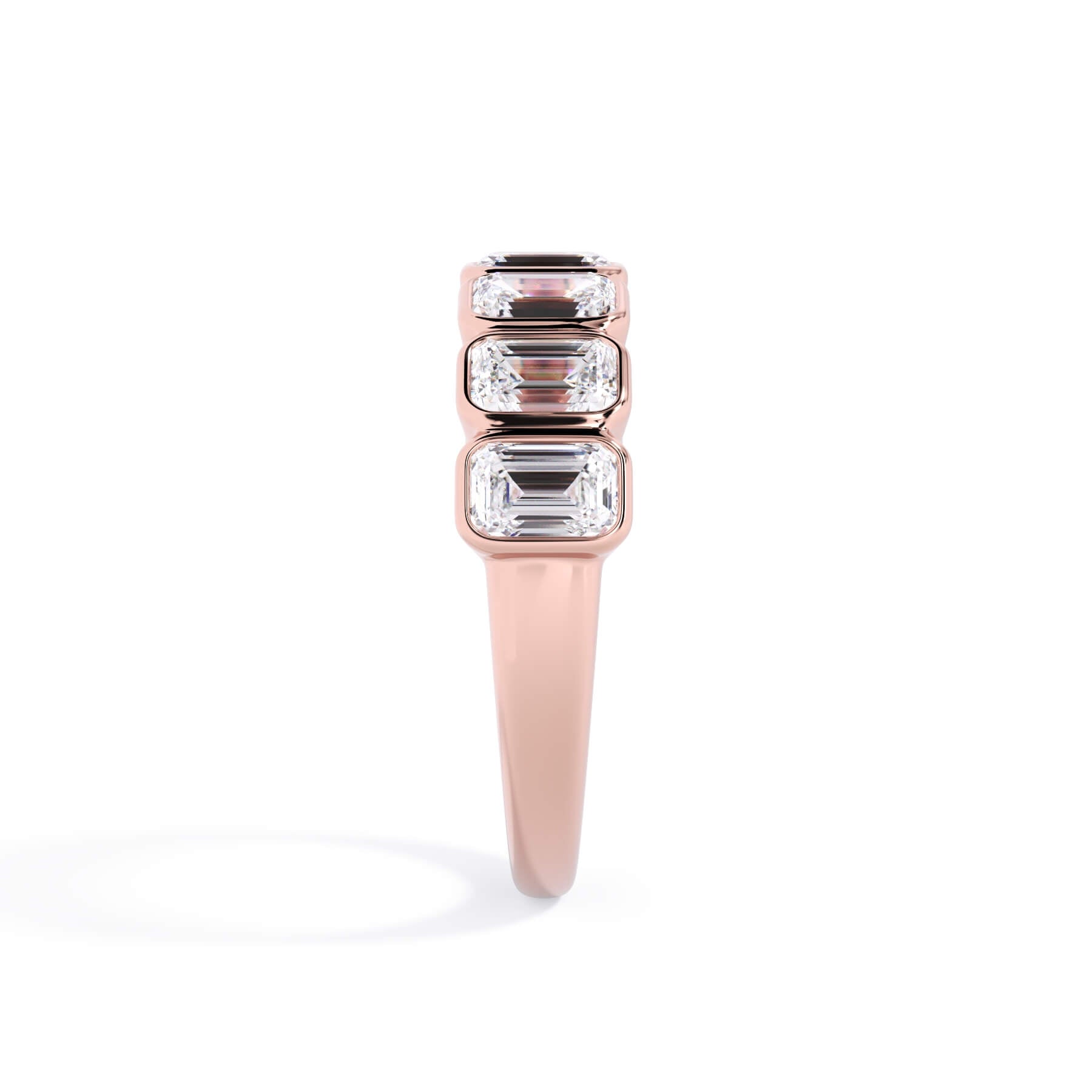 A picture of a seven stone diamond wedding ring with emerald cut diamonds that are bezel set in rose gold on a white background with a side profile view.