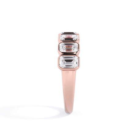 A picture of a seven stone diamond wedding ring with emerald cut diamonds that are bezel set in rose gold on a white background with a side profile view.