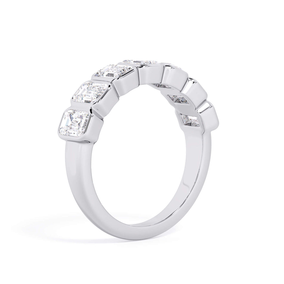 A picture of a seven stone diamond wedding ring with emerald cut diamonds that are bezel set in white gold or platinum on a white background with a slightly angled, through the finger view.