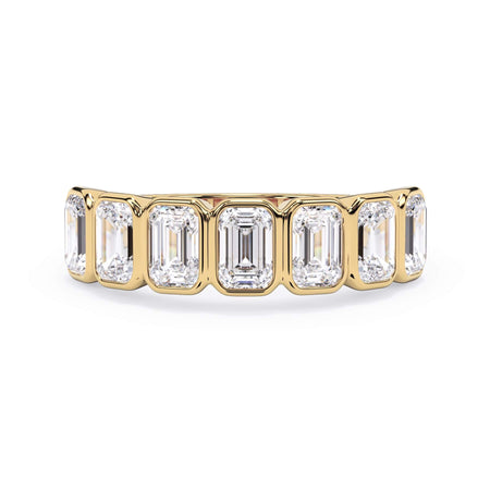 A picture of a seven stone diamond wedding ring with emerald cut diamonds that are bezel set in yellow gold on a white background with the ring facing forward, lying down.