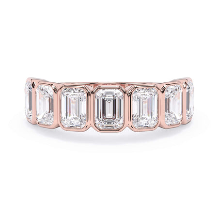 A picture of a seven stone diamond wedding ring with emerald cut diamonds that are bezel set in rose gold on a white background with the ring facing forward, lying down.