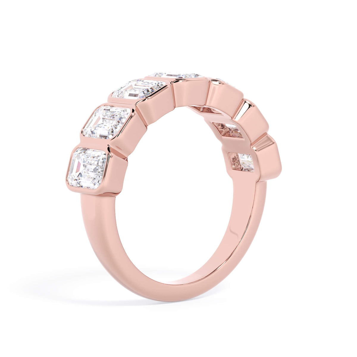 A picture of a seven stone diamond wedding ring with emerald cut diamonds that are bezel set in rose gold on a white background with a slightly angled, through the finger view.