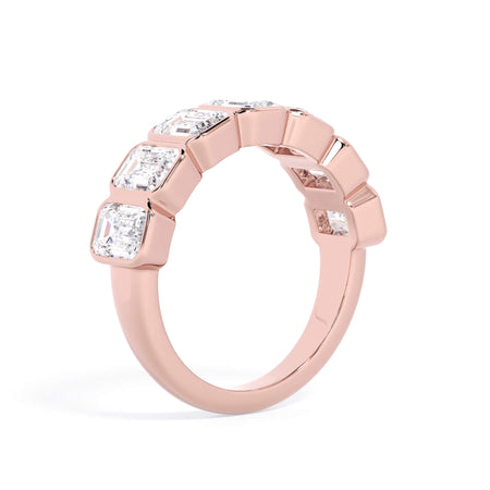 A picture of a seven stone diamond wedding ring with emerald cut diamonds that are bezel set in rose gold on a white background with a slightly angled, through the finger view.